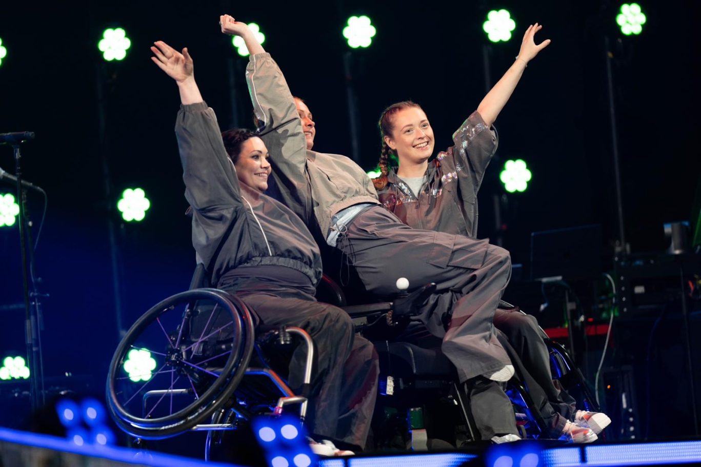 3 wheelchair users in dance poses. Hannah is on the left supporting the middle dancer to raise from her chair