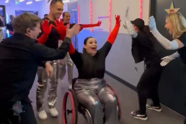 A joyful group celebrates, with Hannah, a woman in a wheelchair, all wearing matching outfits.