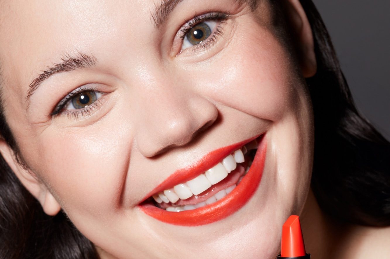Smiling woman with red lipstick holding a lipstick.